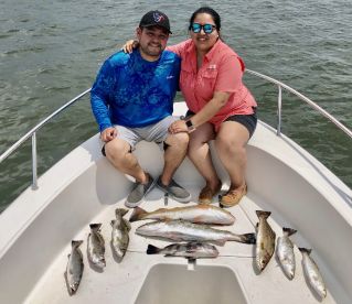 Couple enjoying a successful fishing trip, showcasing a variety of Speckled Trout on the boat.