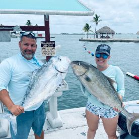 Two anglers proudly displaying their catches, a large Jack Crevalle and a Amberjack, at a scenic dockside location.