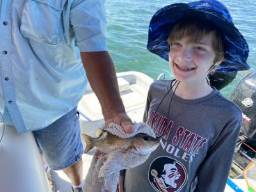A young angler proudly displaying a caught fish while on a fishing trip, showcasing a sunny day on the water.