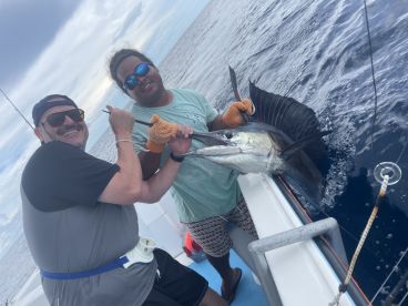 Two anglers proudly displaying a large Sailfish while fishing offshore, showcasing a successful day on the water.