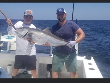 A young angler and an adult proudly displaying a large Amberjack while fishing offshore, showcasing a successful day on the water.