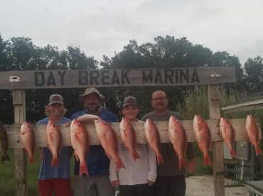 A group of anglers proudly displaying their catch of Red Snapper on a board at Day Break Marina, showcasing a successful fishing trip.
