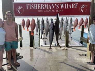 A group of anglers proudly displaying their catch of Snapper and a large Kingfish at Fisherman's Wharf in Port Aransas, Texas.