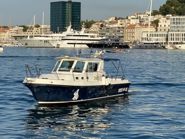 A sleek fishing boat cruising in a vibrant harbor, surrounded by luxury yachts and coastal buildings.