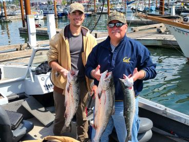 Two anglers proudly displaying their catch of Salmon while aboard a fishing boat at the marina.