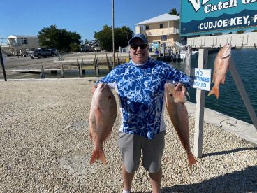 Angler proudly displaying two large Snapper at the dock in Cudjoe Key, showcasing a successful fishing trip.
