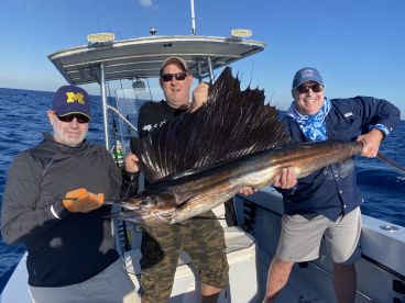 Three anglers proudly displaying a large Sailfish aboard a fishing boat in open waters.
