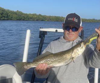 An angler proudly displaying a large Speckled Trout while fishing in a scenic coastal environment.