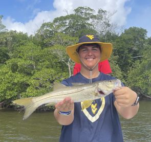A young angler proudly displaying a Snook caught while fishing in a lush mangrove environment.
