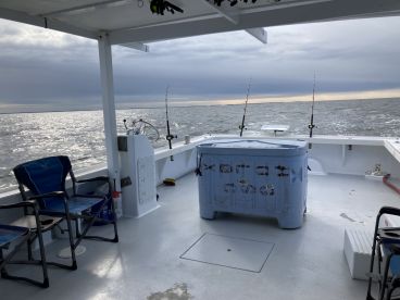 Interior view of a fishing boat showcasing seating and fishing gear, set against a backdrop of a calm sea under a cloudy sky.