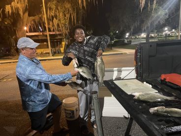 A young angler and an adult proudly displaying their catch of striped bass at night, showcasing a successful fishing trip.