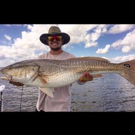 Angler proudly displaying a large Redfish while fishing in open waters, showcasing a beautiful day with clear skies.