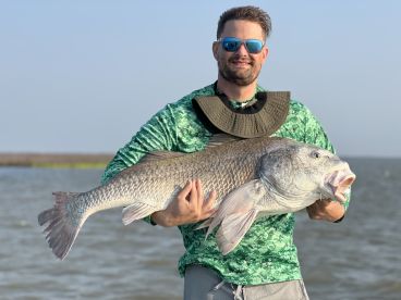 Angler proudly displaying a large Redfish while fishing in a coastal environment.
