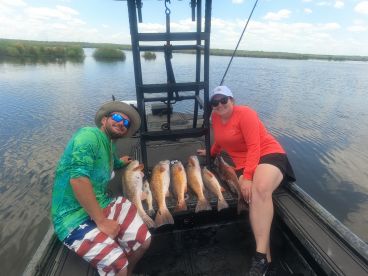 Two anglers proudly displaying their catch of Redfish while enjoying a day on the water in a scenic fishing environment.