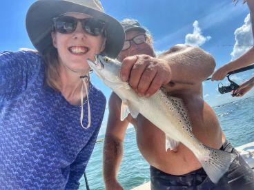 Two anglers smiling while holding a Speckled Trout on a sunny day out on the water.