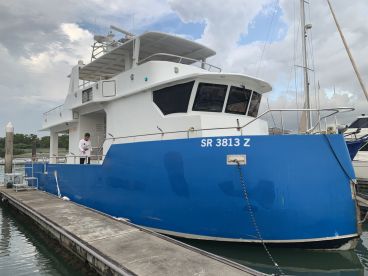 A fishing charter boat docked at the marina, showcasing its blue exterior and spacious design, with a crew member preparing for the next trip.