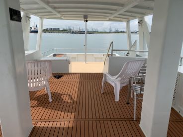 Interior view of a spacious boat deck featuring comfortable seating and a scenic waterfront backdrop.