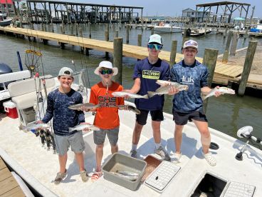 A group of young anglers proudly displaying their catch of Speckled Trout at the dock after a successful fishing trip.