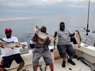 Three anglers proudly displaying their catch of large Lake Trout while fishing on a calm lake.