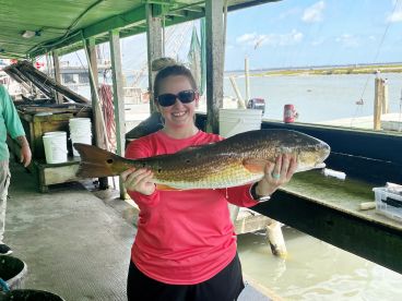 An angler proudly displaying a large Redfish at a fishing dock, showcasing a successful catch during a coastal fishing trip.