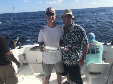 A young angler proudly displaying a Barracuda while fishing on a charter boat in open waters.