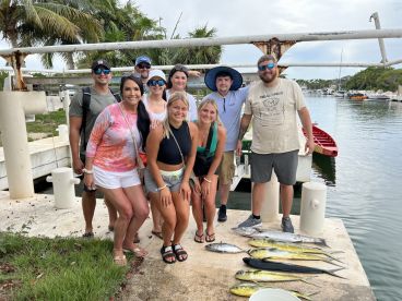 A group of anglers proudly displaying their catch of Mahi Mahi and other species at the dock after a successful fishing trip.