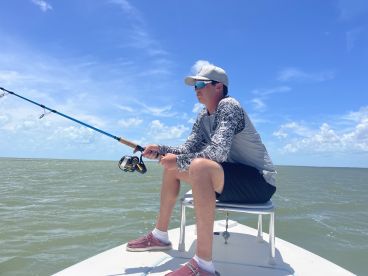 A young angler focused on fishing from a boat in calm waters under a clear blue sky.