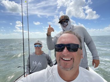 Three anglers enjoying a day on the water, with a scenic backdrop of the ocean and clouds, showcasing the camaraderie of a fishing trip.
