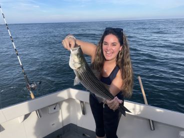A happy angler proudly displaying a striped bass while fishing on a boat, showcasing a beautiful day on the water.
