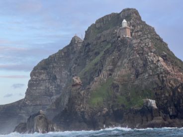 A scenic view of a rugged coastal cliff featuring a lighthouse, captured during a boat trip.
