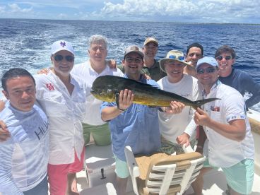 A group of anglers proudly displaying a large Mahi Mahi aboard a fishing charter in sunny waters.