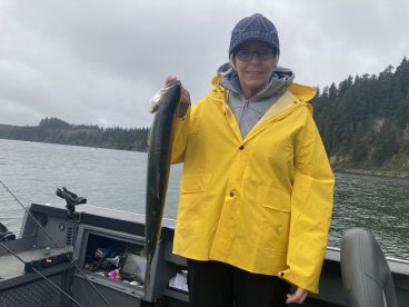 An angler proudly displaying a large Salmon while fishing in a scenic coastal environment, wearing a bright yellow rain jacket.