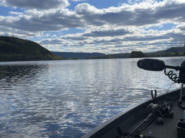 A scenic view of a fishing boat on a calm river, surrounded by lush hills and a dramatic sky, ideal for a peaceful fishing experience.