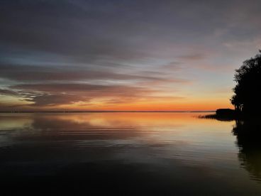 A serene sunset over calm waters, reflecting vibrant colors in the sky, creating a picturesque fishing environment.
