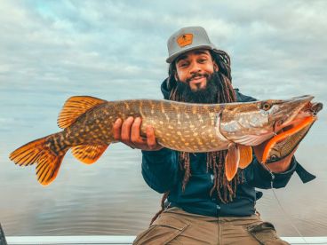 An angler proudly displaying a large Northern Pike while fishing on a calm lake, showcasing the thrill of freshwater fishing.