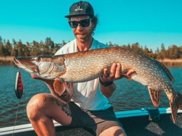 Angler proudly displaying a large Northern Pike while fishing on a serene lake.