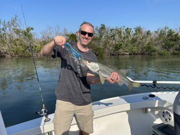 An angler proudly displaying a Snook caught while fishing in a scenic mangrove area.