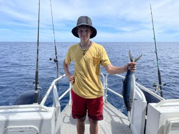 A young angler proudly displaying a caught fish while aboard a fishing boat in open waters.