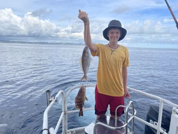 A young angler proudly displaying two freshly caught fish while aboard a fishing boat in open waters.