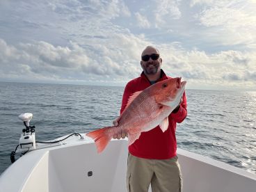 Angler proudly displaying a large Red Snapper while fishing offshore, showcasing a successful day on the water.