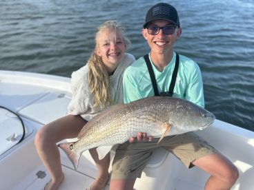 Two young anglers proudly displaying a large Redfish while enjoying a day on the water.