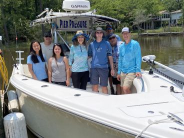 A cheerful group of anglers posing on the side of the 'Pier Pressure' boat, ready for a day of fishing in a scenic waterway.
