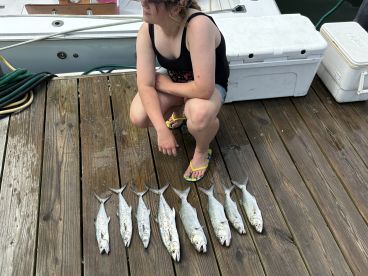 A young angler sits beside a neat display of several fish on a wooden dock, showcasing a successful fishing trip.
