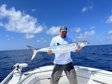 Angler proudly displaying a large King Mackerel while aboard a fishing boat in open waters.