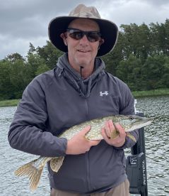 Angler proudly displaying a Northern Pike while fishing in a scenic freshwater environment.