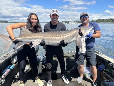 Three anglers proudly displaying a large Sturgeon on a fishing boat, showcasing their successful catch during a day on the water.