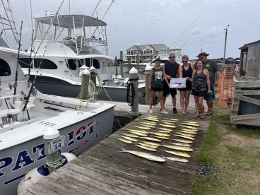 A group of anglers proudly displaying their catch of Mahi Mahi on a dock after a successful fishing trip aboard the 'Patriot'.