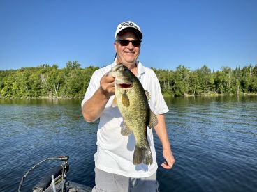 An adult angler proudly displaying a large Largemouth Bass while fishing on a serene lake surrounded by lush greenery.
