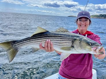Angler proudly displaying a large Striped Bass while fishing on a boat, showcasing a beautiful day on the water.