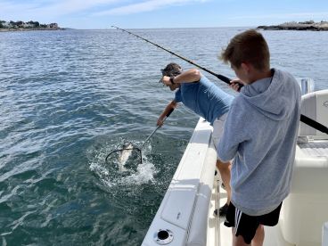 A young angler assists an adult in landing a fish while fishing from a boat, showcasing an exciting moment on the water.